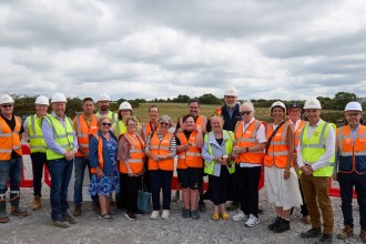A group of around twenty people in hi-vis vests and hard hats at the Gowerton solar farm site, with panel mounting frames in the fields behind