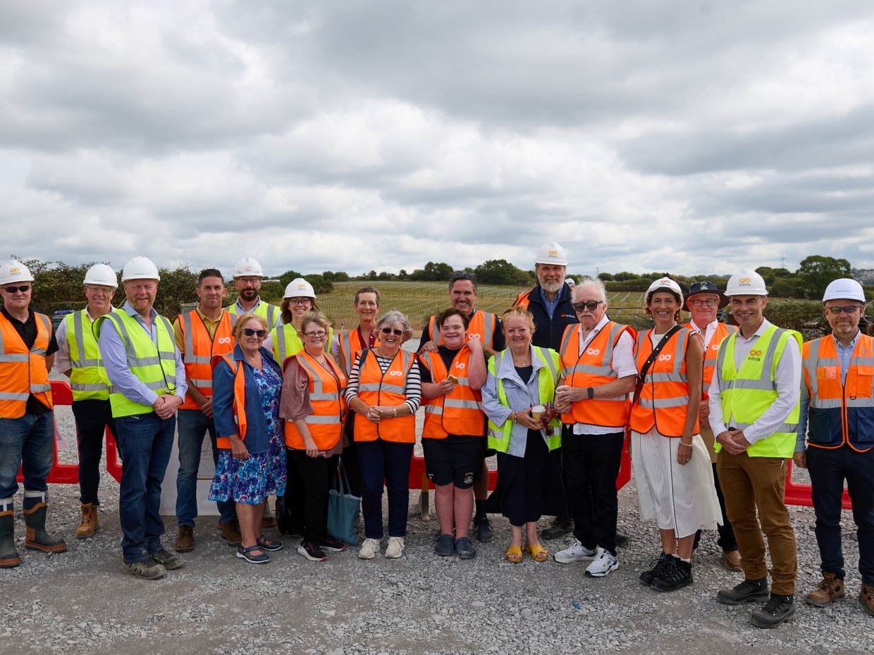 A group of around twenty people in hi-vis vests and hard hats at the Gowerton solar farm site, with panel mounting frames in the fields behind