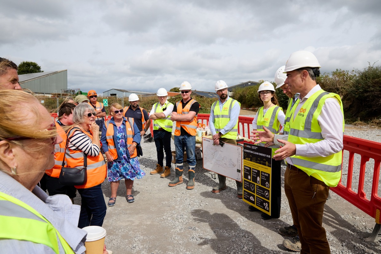Bruce Heppenstall in a hard hat and hi-vis vest speaking to a group of visitors beside a Gowerton Clean Energy Hub information board
