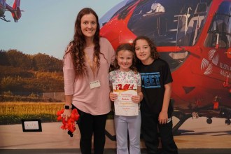 Emma Kinnear with her daughter Gracie holding a Child of Wales certificate and her son Chester at the Wales Air Ambulance base