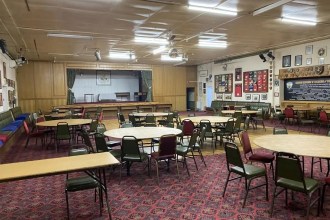 The Great Mountain club's main hall, with round tables, a stage and rugby honours boards on the walls