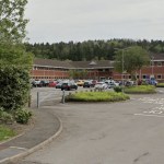 The entrance to HM Land Registry's Swansea office, with a bilingual sign beside the access road and the red-brick office building behind a car park