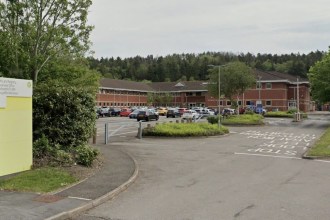 The entrance to HM Land Registry's Swansea office, with a bilingual sign beside the access road and the red-brick office building behind a car park