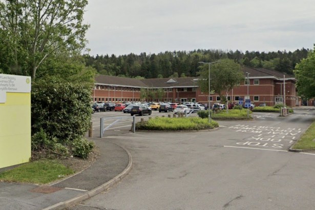The entrance to HM Land Registry's Swansea office, with a bilingual sign beside the access road and the red-brick office building behind a car park