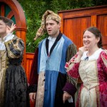 Three actors in Elizabethan costume on Illyria's outdoor stage, one in a patchwork jester's outfit and cap