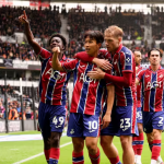 Swansea City players celebrating a goal in their red and blue away kit at Pride Park