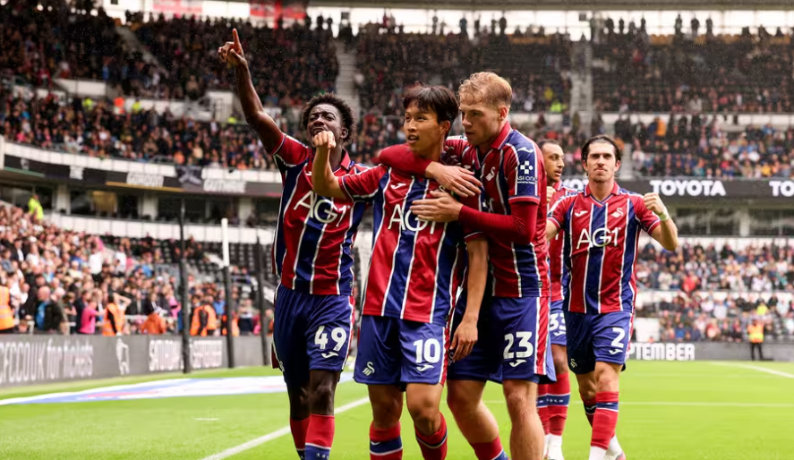 Swansea City players celebrating a goal in their red and blue away kit at Pride Park