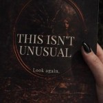 A hand holding a copy of the psychological horror collection This Isn't Unusual by A. Sjoberg against dark undergrowth