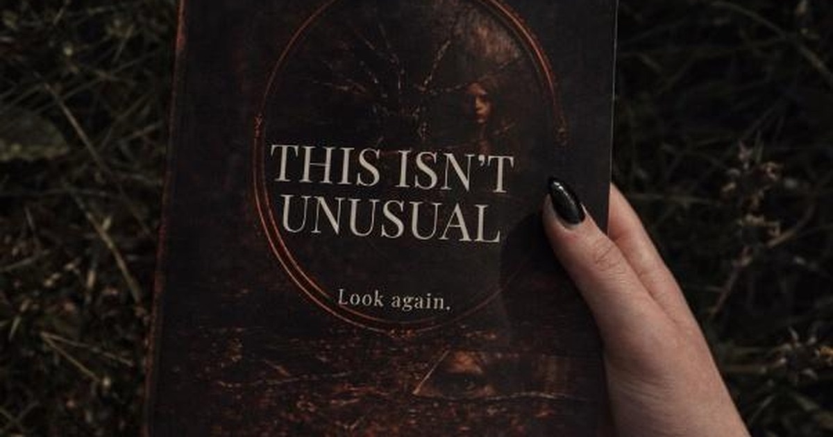 A hand holding a copy of the psychological horror collection This Isn't Unusual by A. Sjoberg against dark undergrowth