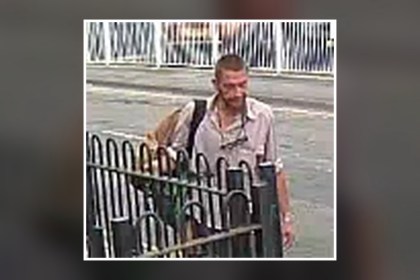 An RSPCA appeal image of a man standing behind black railings on a street, wearing a light shirt and carrying a bag on his shoulder
