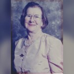 Studio portrait of Mair Lloyd of Llangunnor, smiling, wearing glasses and a pale blouse