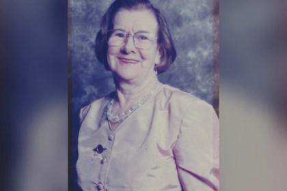 Studio portrait of Mair Lloyd of Llangunnor, smiling, wearing glasses and a pale blouse