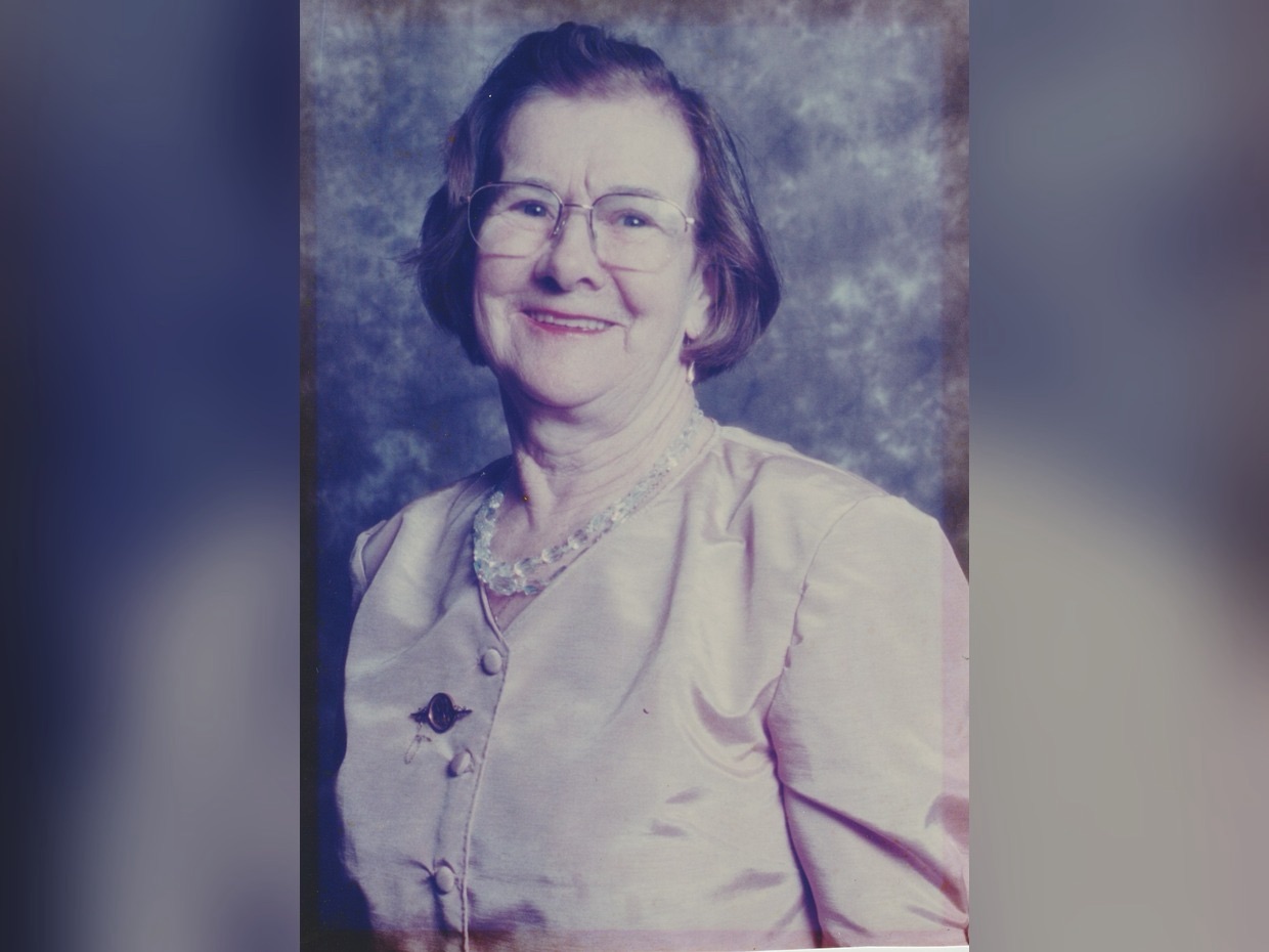 Studio portrait of Mair Lloyd of Llangunnor, smiling, wearing glasses and a pale blouse