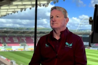 Scarlets managing director Jon Daniels sitting in the stand at Parc y Scarlets with the pitch behind him