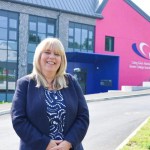 Kelly Fountain standing in front of the redeveloped Gorseinon campus entrance with the college's pink signage behind her