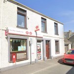 The white-fronted Kidwelly Post Office on Station Road, with bilingual Post Office signage, a red wall postbox and Welsh flag bunting in the window
