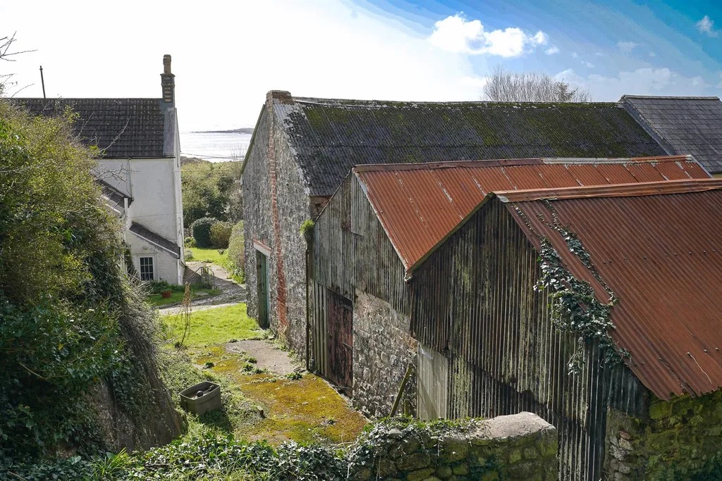 Stone barns with corrugated iron roofs behind the house, with the sea beyond