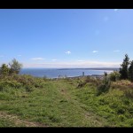 View from the grassy summit of Kilvey Hill over Swansea city centre and the curve of Swansea Bay towards Mumbles under a blue sky