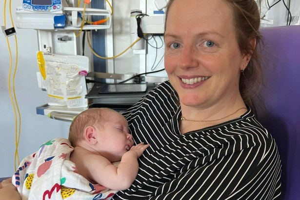 Kirsten smiling as baby Olive sleeps on her chest in a hospital chair