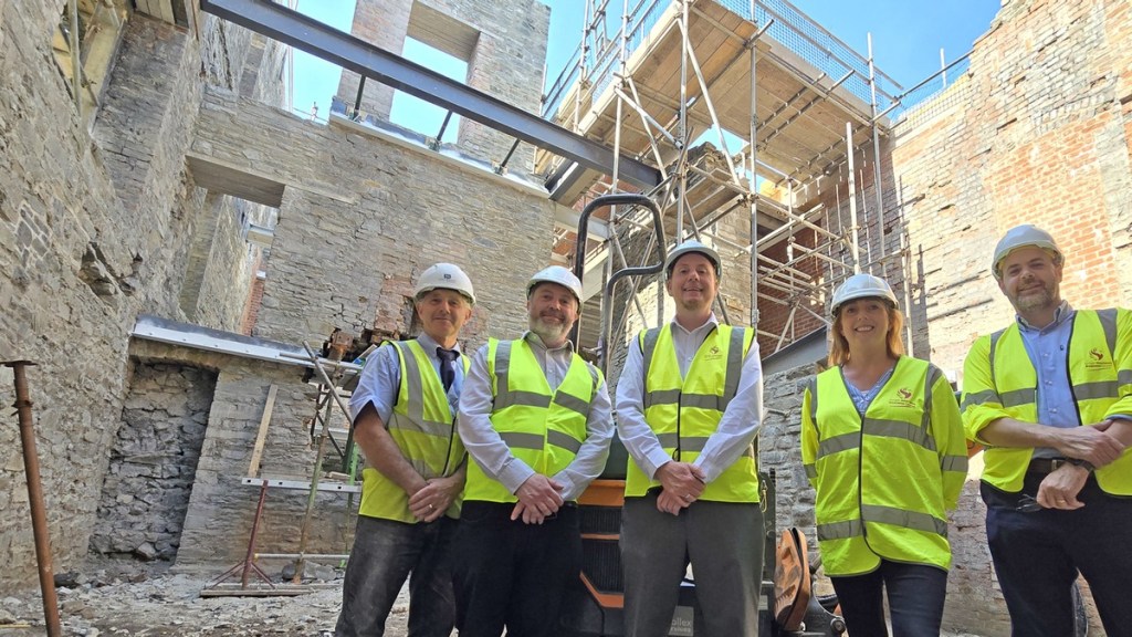 Five people in hi-vis vests and hard hats stand inside the stone shell of the Laboratory Building during reconstruction