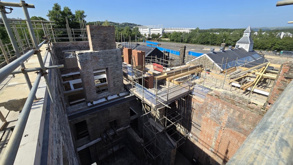 View from scaffolding on top of the Laboratory Building across brick chimney stacks towards the Swansea.com Stadium and a clock tower