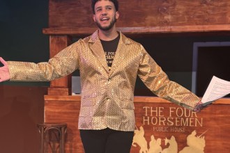 Dylan Fairbairn in a gold sequinned jacket with arms spread wide in front of The Four Horsemen pub set, holding a quiz sheet