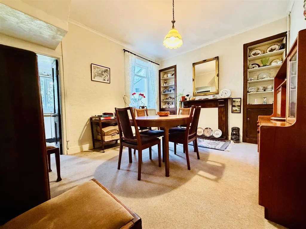 A dining room with a wooden table and chairs, display cabinets and a mirror over the fireplace
