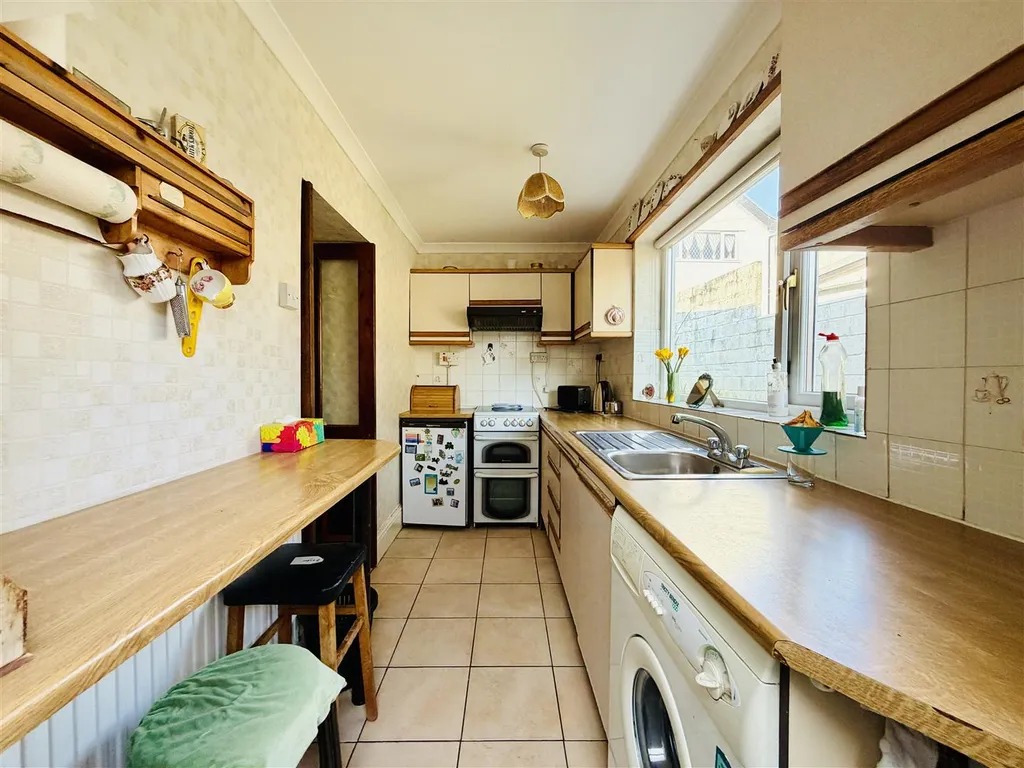 A narrow galley kitchen with wooden worktops, original wall units and a tiled floor