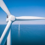 Offshore wind turbines at sea viewed from above, with a turbine hub and blades in the foreground