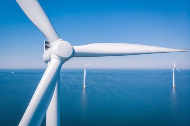 Offshore wind turbines at sea viewed from above, with a turbine hub and blades in the foreground