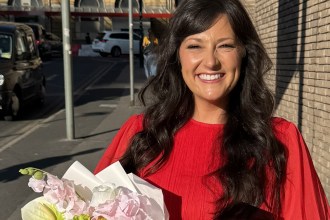 Lucy Hellyer Jones in a red dress holding a bouquet and the 2026 Hair and Beauty Awards Best Home Salon trophy outside the AO Arena