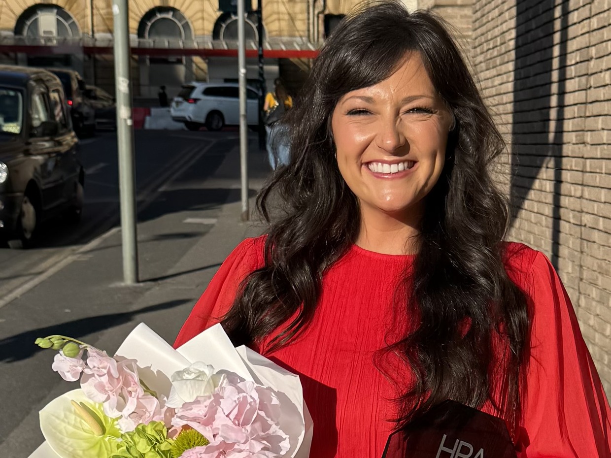 Lucy Hellyer Jones in a red dress holding a bouquet and the 2026 Hair and Beauty Awards Best Home Salon trophy outside the AO Arena
