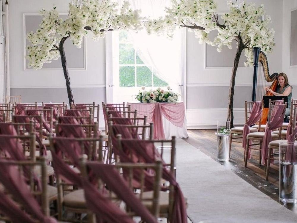 A harpist plays beside blossom trees in a ceremony room laid out with chairs at Manor Park