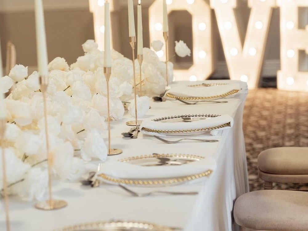 A wedding table laid with white roses and candles in front of illuminated LOVE letters at Manor Park