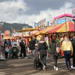 Crowds walking between stalls and rides at the Neath Great Fair funfair on Milland Road, with hills behind