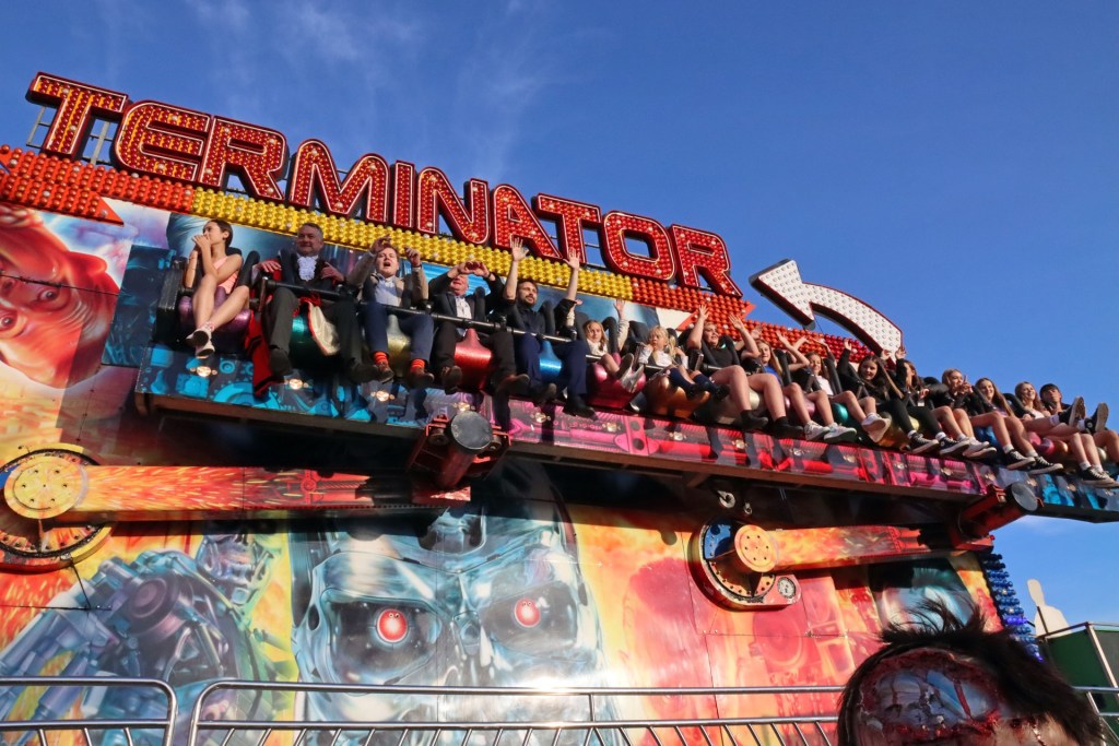 Riders with arms in the air on the Terminator ride at Neath Great Fair, under a blue sky