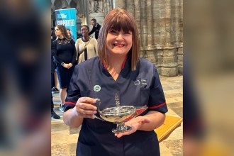 Nicola Lewis in NHS Wales nursing uniform smiling and holding the ceremonial Nightingale lamp inside Westminster Abbey