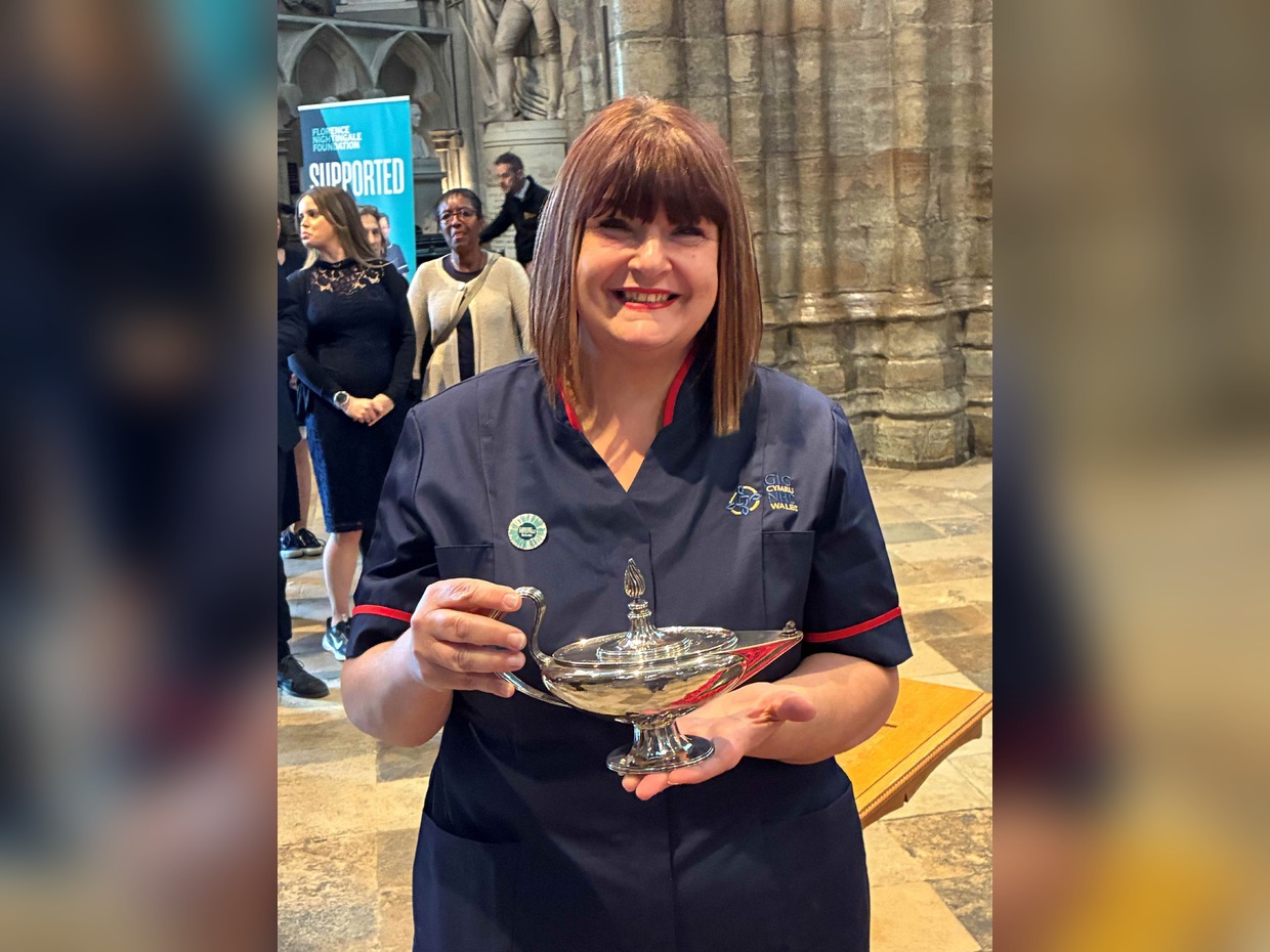 Nicola Lewis in NHS Wales nursing uniform smiling and holding the ceremonial Nightingale lamp inside Westminster Abbey