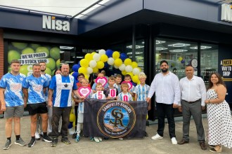 Sandfields Rangers players holding a banner and cheque hearts outside the new Nisa store in Port Talbot with the owners and balloons