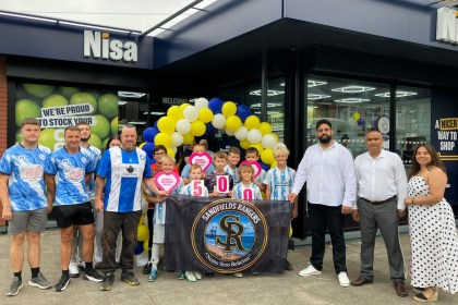 Sandfields Rangers players holding a banner and cheque hearts outside the new Nisa store in Port Talbot with the owners and balloons