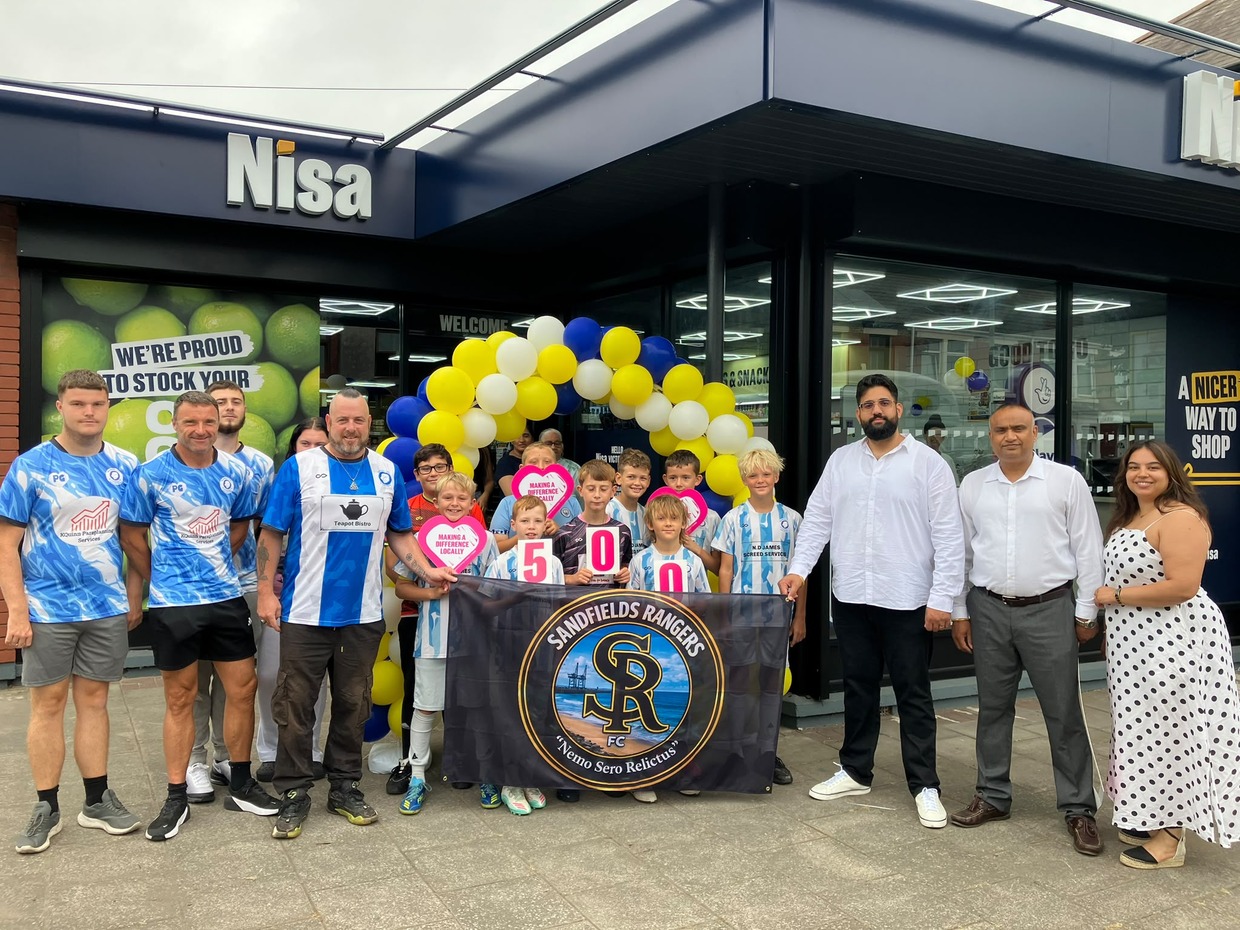 Sandfields Rangers players holding a banner and cheque hearts outside the new Nisa store in Port Talbot with the owners and balloons
