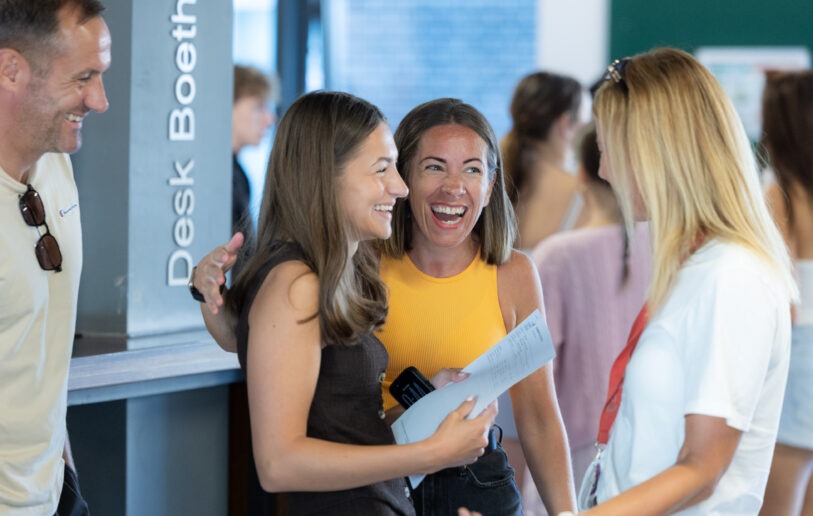 A student and family members laugh together beside a bilingual results desk at NPTC Group of Colleges
