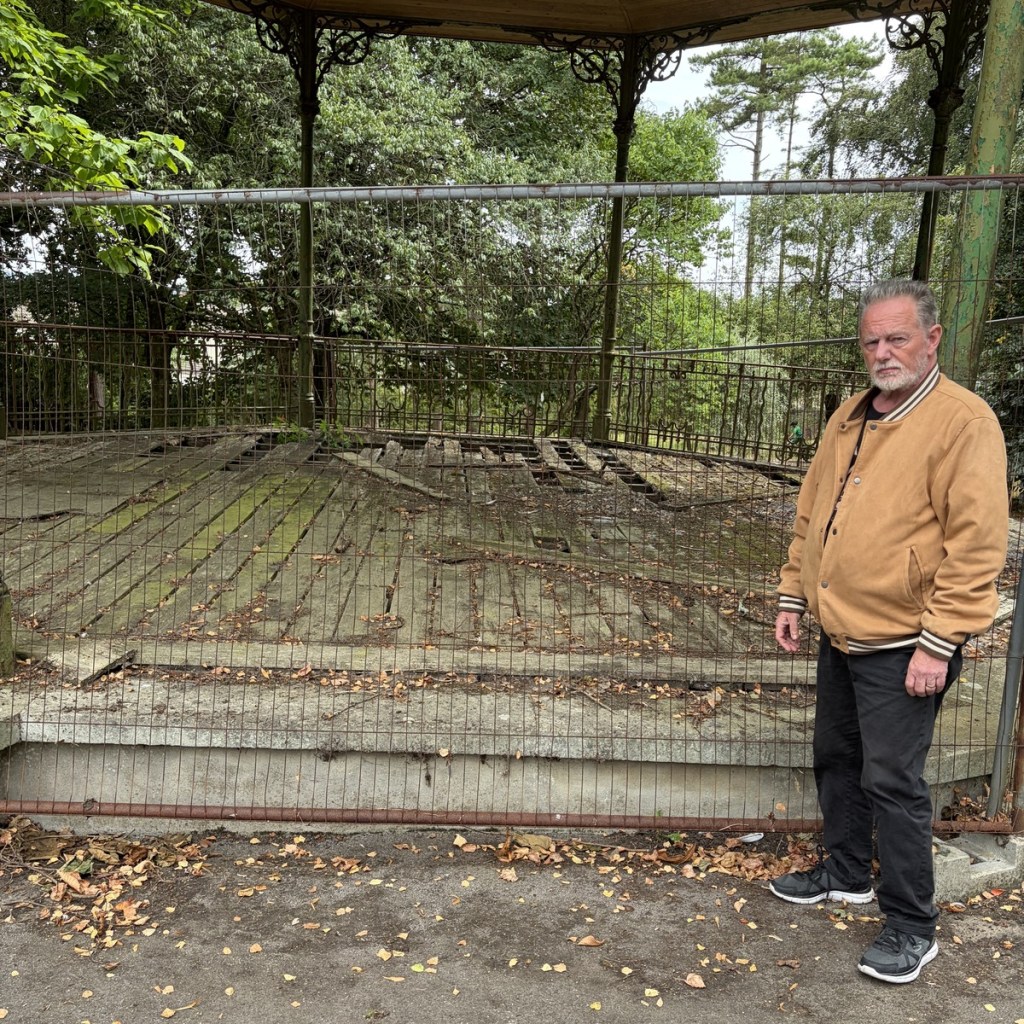 Steel mesh fencing surrounds Parc Howard’s bandstand, its wooden floor rotted and broken in places, with a man standing beside it
