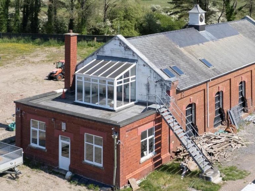 The red-brick Old Pump House at Pembrey with its white clock tower, windows boarded and a steel staircase against one wall