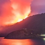 Orange smoke rising from a burning hillside above the lit shopfronts on Pendine seafront