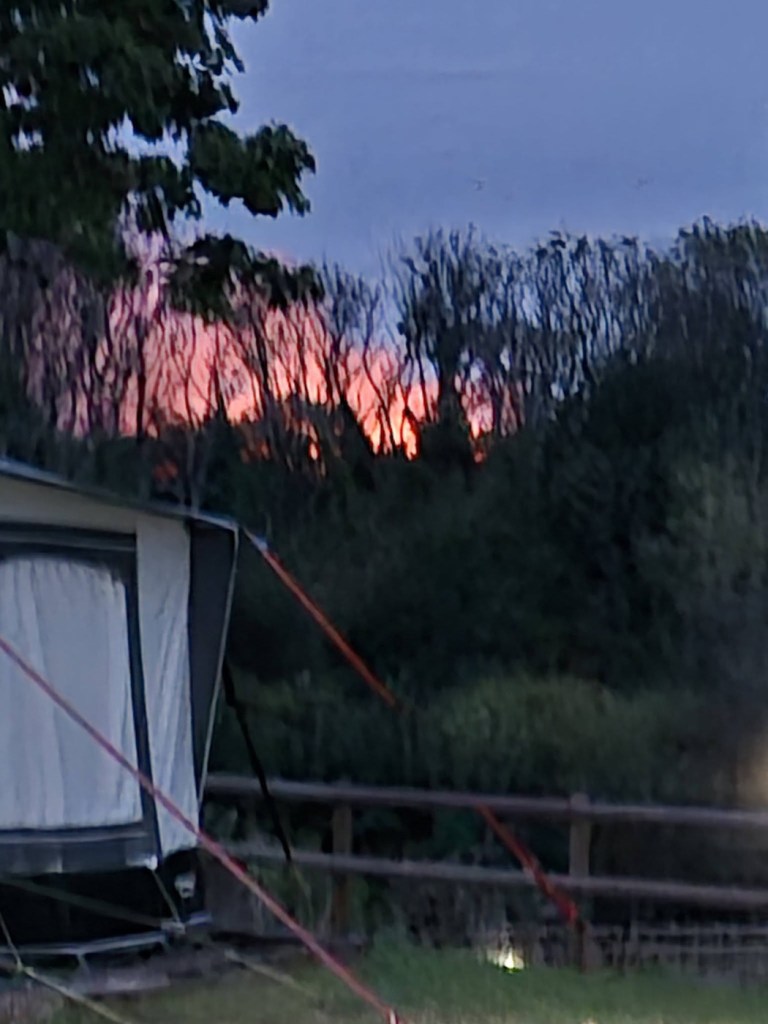 Fire glowing through a line of trees behind a caravan awning at night