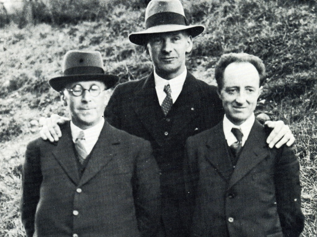 Black and white photograph of three men in suits and hats standing together on a hillside in the 1930s