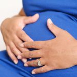 A pregnant woman's hands resting on her bump, wearing a ring and a watch
