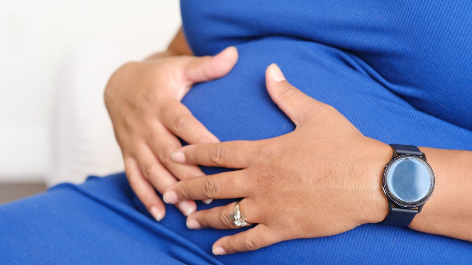A pregnant woman's hands resting on her bump, wearing a ring and a watch