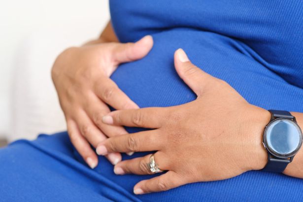 A pregnant woman's hands resting on her bump, wearing a ring and a watch